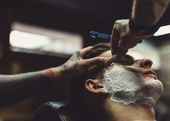 crop-stylish-applying-foam-customer-s-cheeks-shaving-while-working-barbershop